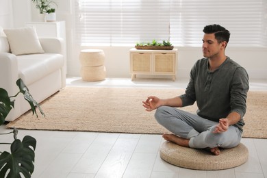 Photo of Man meditating on wicker mat at home. Space for text