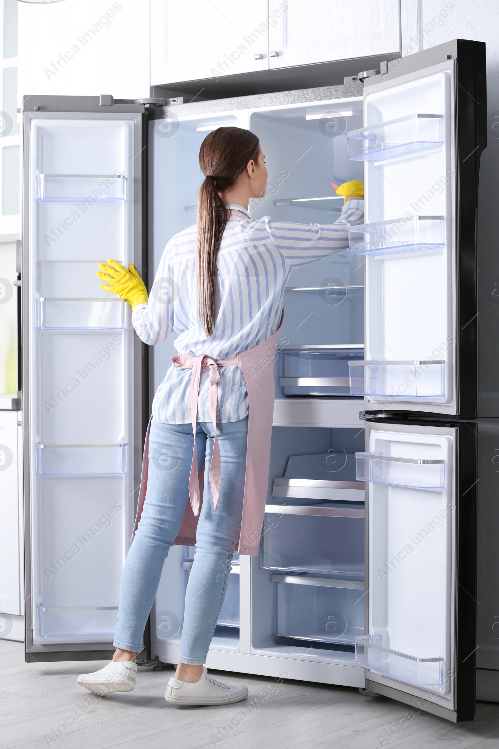 Photo of Woman in rubber gloves cleaning refrigerator at home