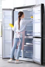 Woman in rubber gloves cleaning refrigerator at home