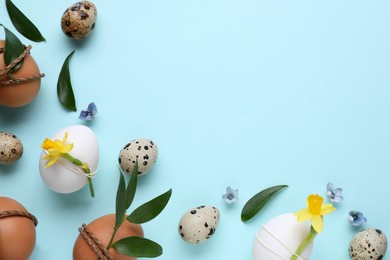 Easter eggs decorated with green leaves and flowers on light blue background, flat lay. Space for text