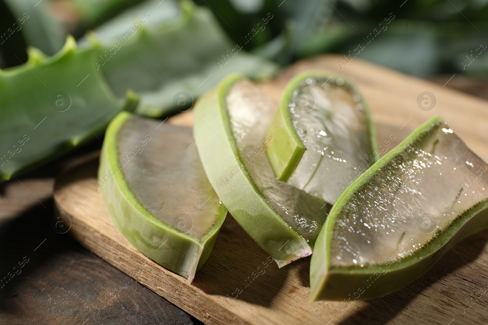 Photo of Slices of fresh aloe vera leaves with gel on wooden table, closeup