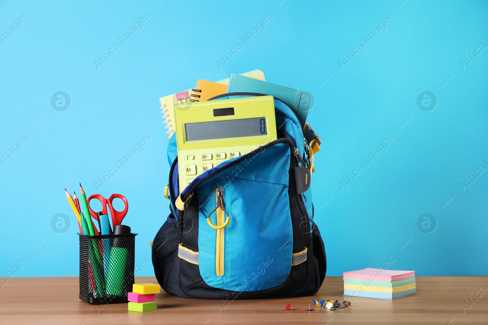 Photo of Backpack and different school stationery on wooden table against light blue background