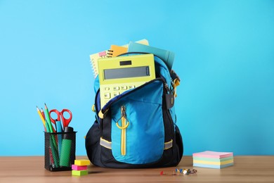 Photo of Backpack and different school stationery on wooden table against light blue background