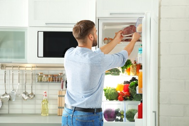 Photo of Man taking fresh meat out of refrigerator in kitchen