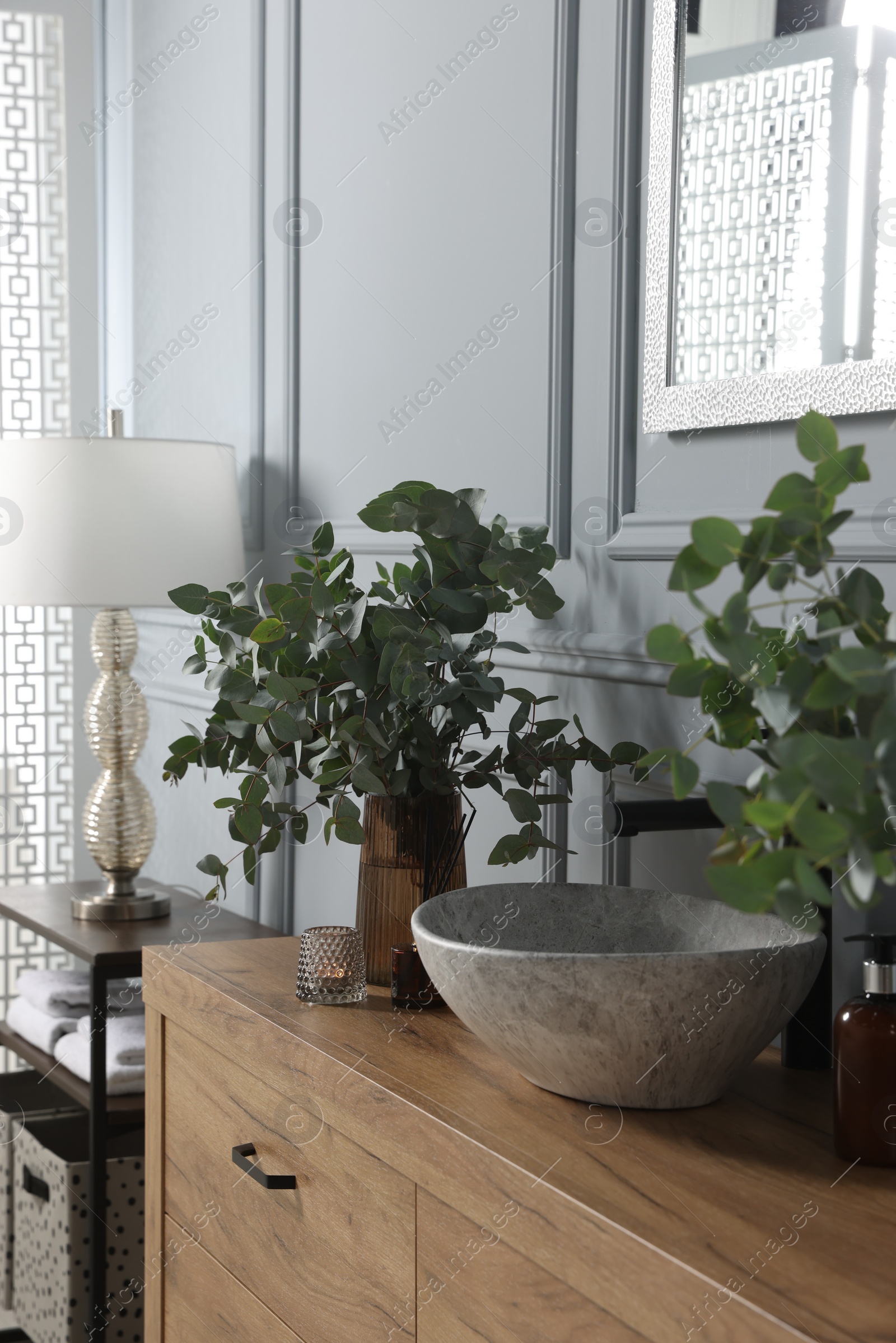 Photo of Eucalyptus branches near vessel sink on bathroom vanity. Interior design