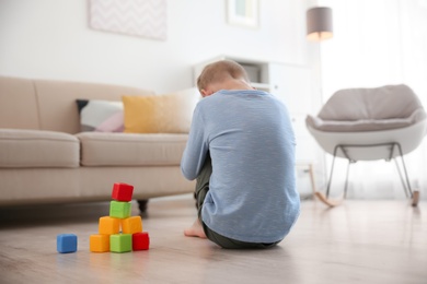 Photo of Lonely little boy with cubes sitting on floor at home. Autism concept