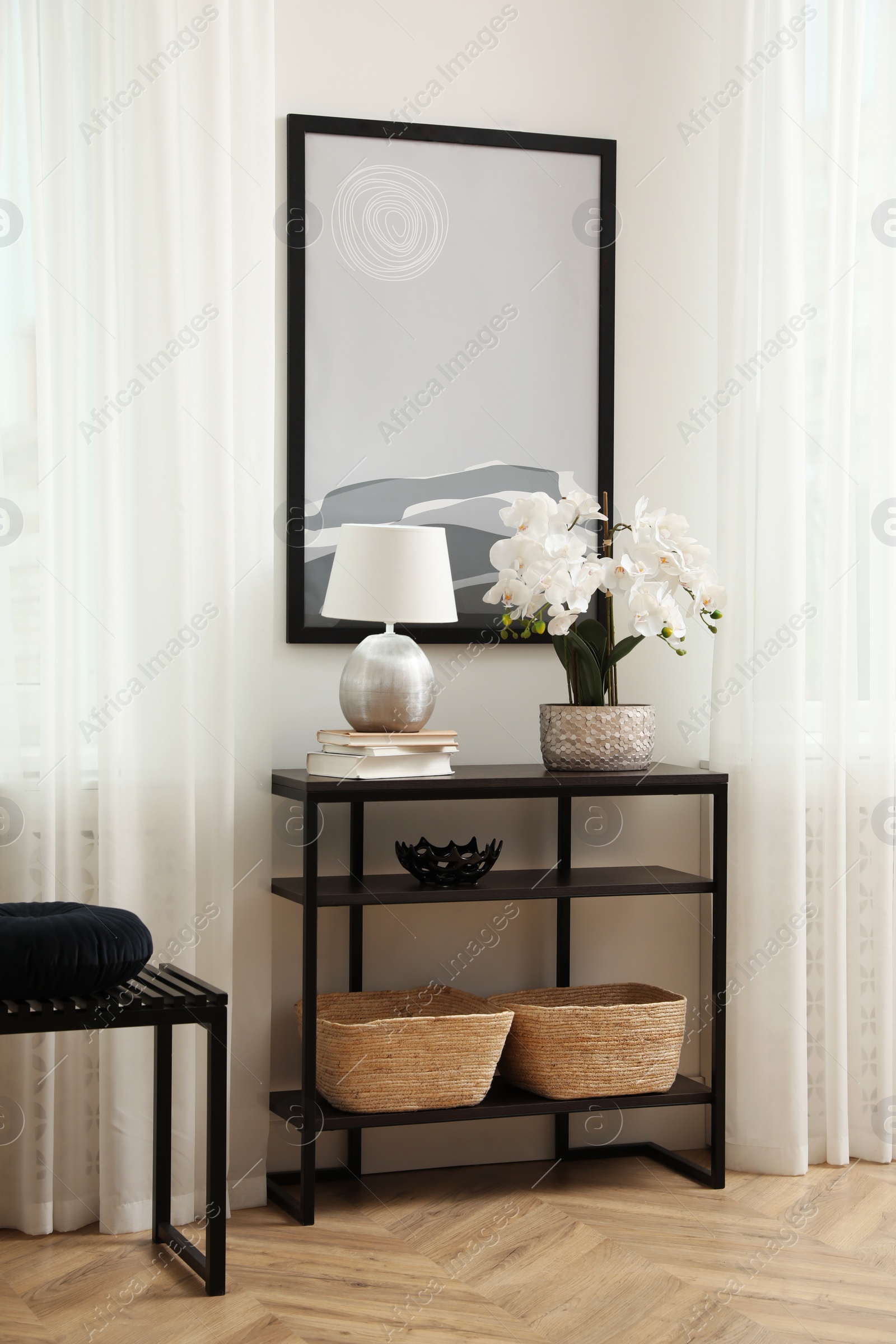 Photo of Blooming orchid and lamp on console table indoors. Interior design