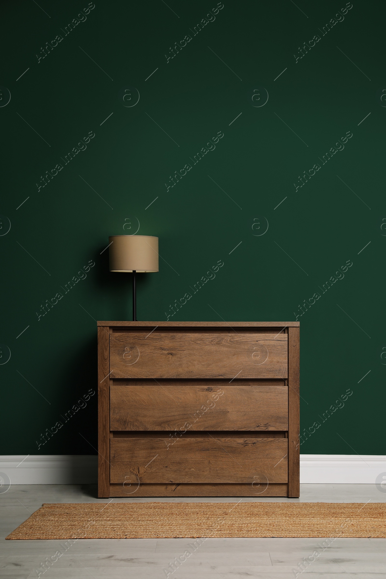 Photo of Modern wooden chest of drawers with lamp near green wall indoors