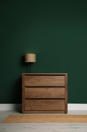 Photo of Modern wooden chest of drawers with lamp near green wall indoors