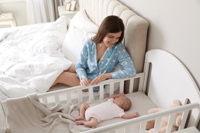 Photo of Happy young mother near crib with sleeping newborn baby in bedroom
