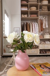 Photo of Bouquet of peony flowers on table in wardrobe room. Interior design