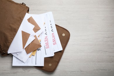 Photo of Brown postman bag with newspapers and mails on white wooden table, flat lay. Space for text