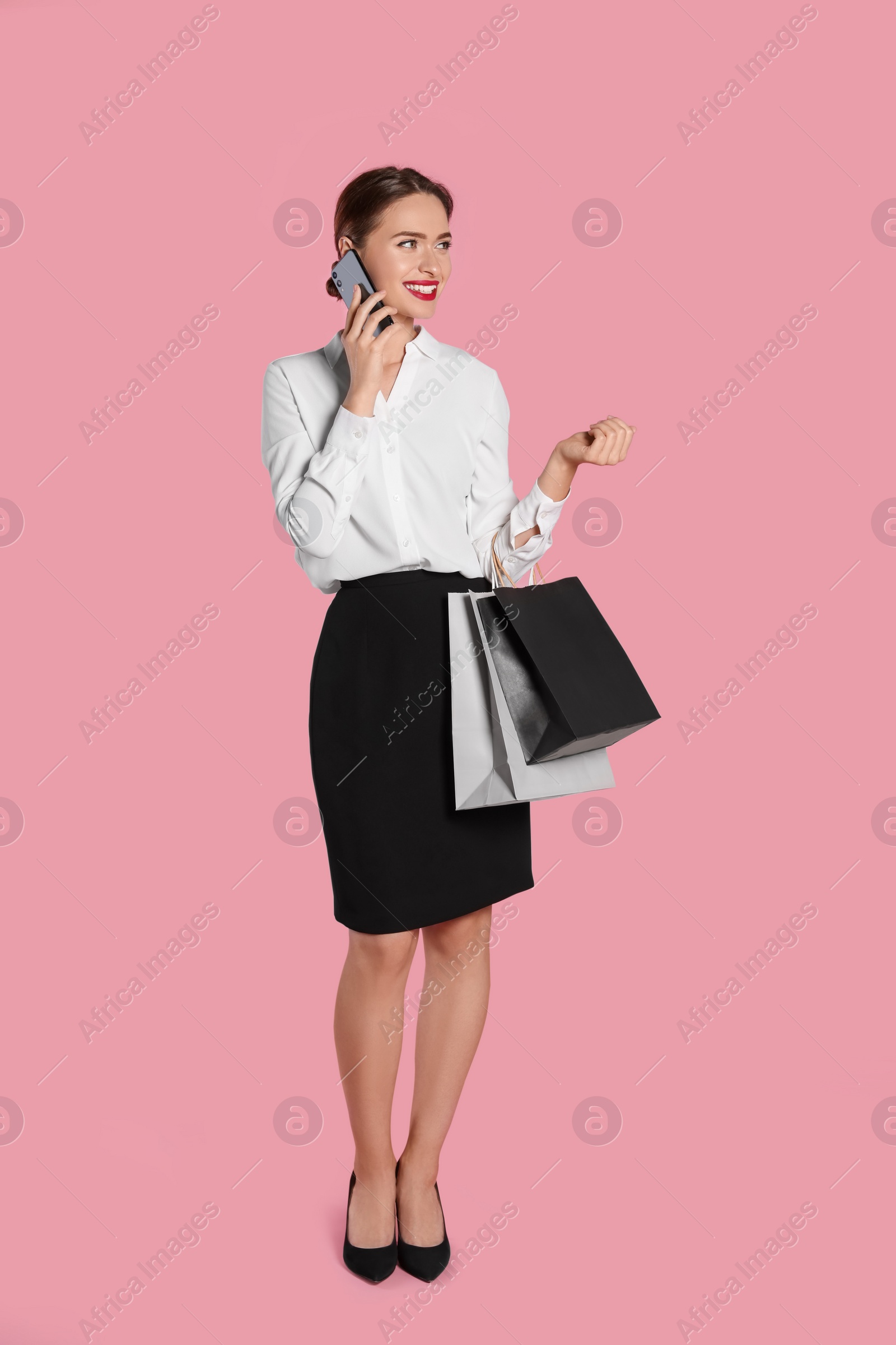 Photo of Happy young woman with shopping bags and smartphone on light pink background. Big sale