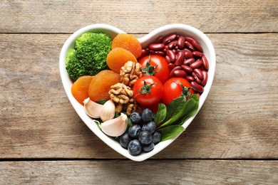 Photo of Bowl with products for heart-healthy diet on wooden background, top view