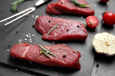 Fresh raw meat steaks and spices on black table, closeup