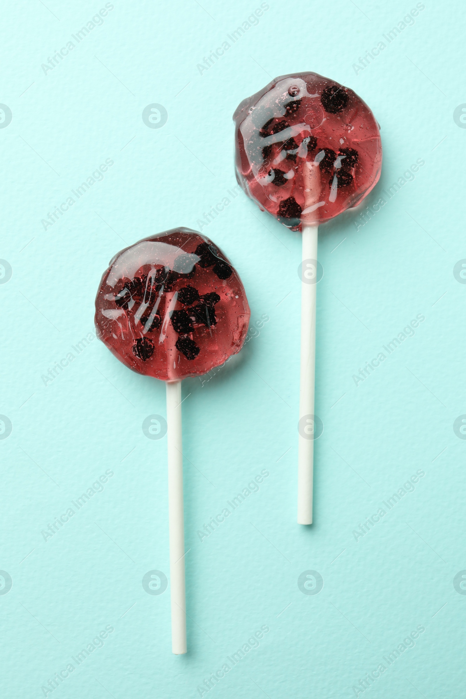 Photo of Sweet colorful lollipops with berries on turquoise background, flat lay