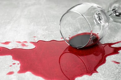 Photo of Overturned glass with red wine spill on grey table, closeup