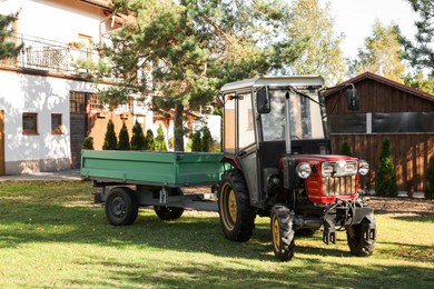 Photo of Modern tractor with empty trailer on green lawn outdoors