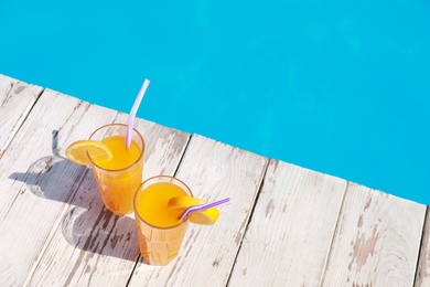 Photo of Refreshing cocktails near outdoor swimming pool on sunny day. Space for text