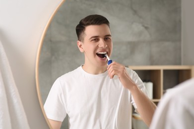 Man brushing his teeth with electric toothbrush near mirror in bathroom