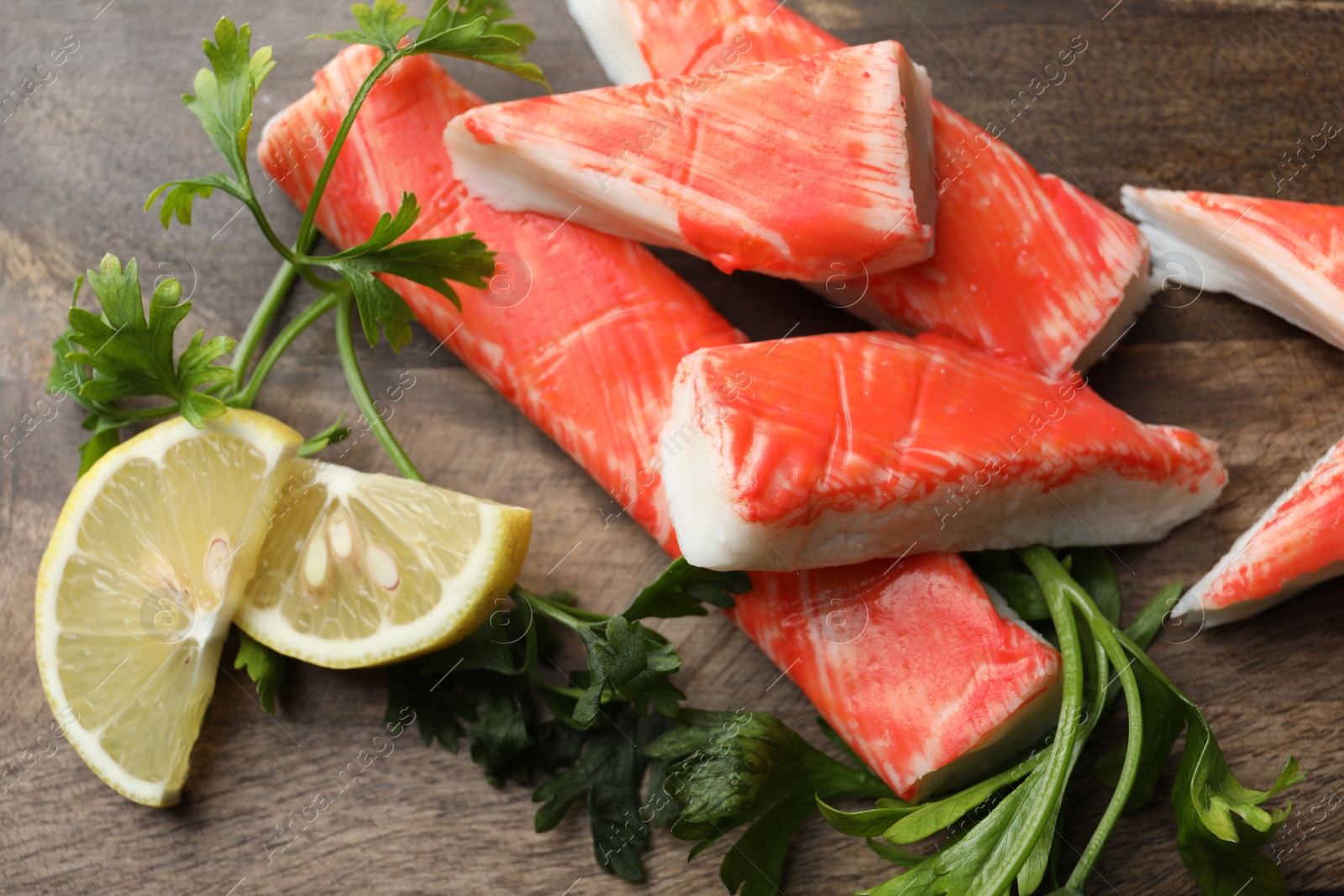 Photo of Crab sticks, lemon slices and parsley on wooden board, closeup