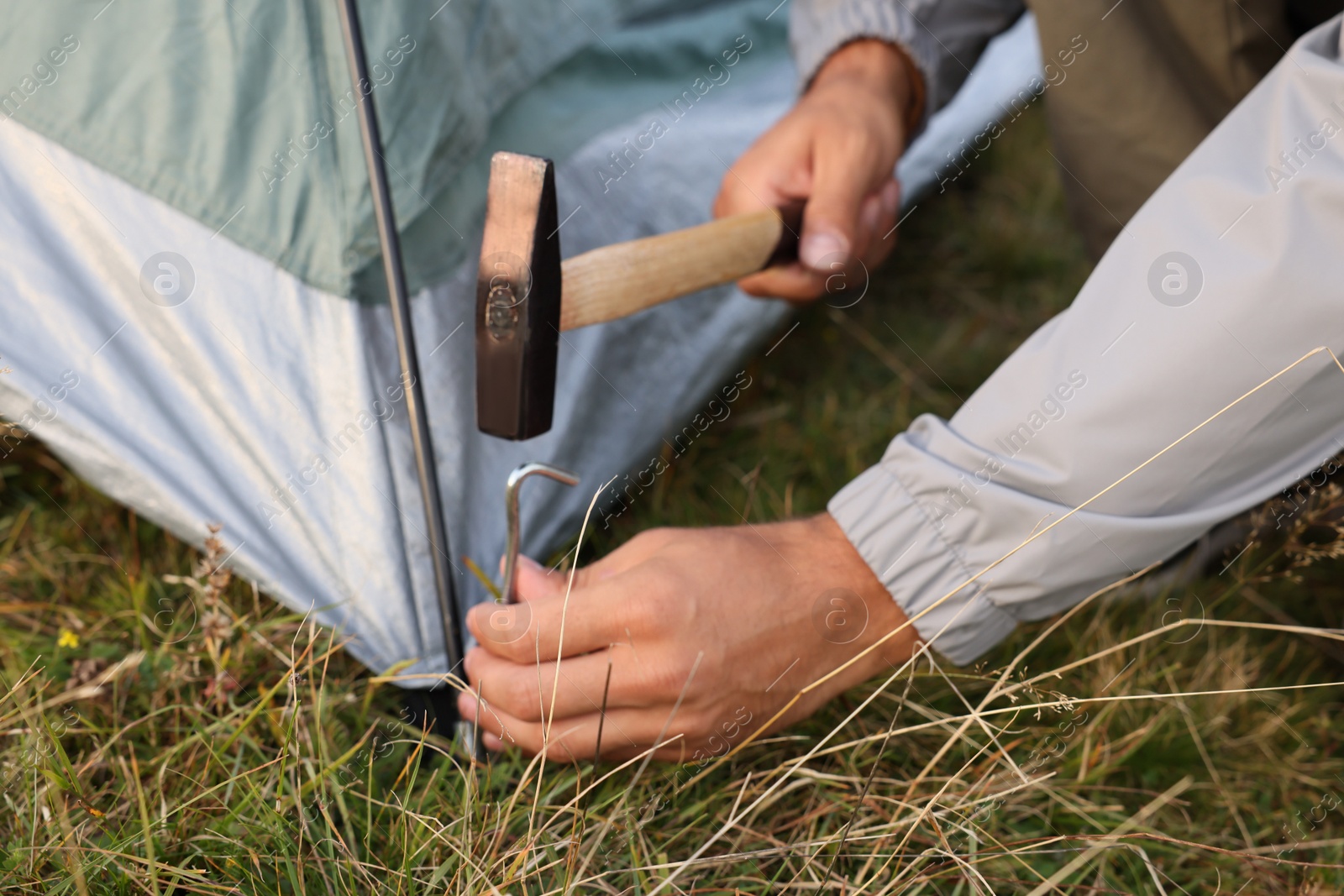 Photo of Man setting up camping tent outdoors, closeup