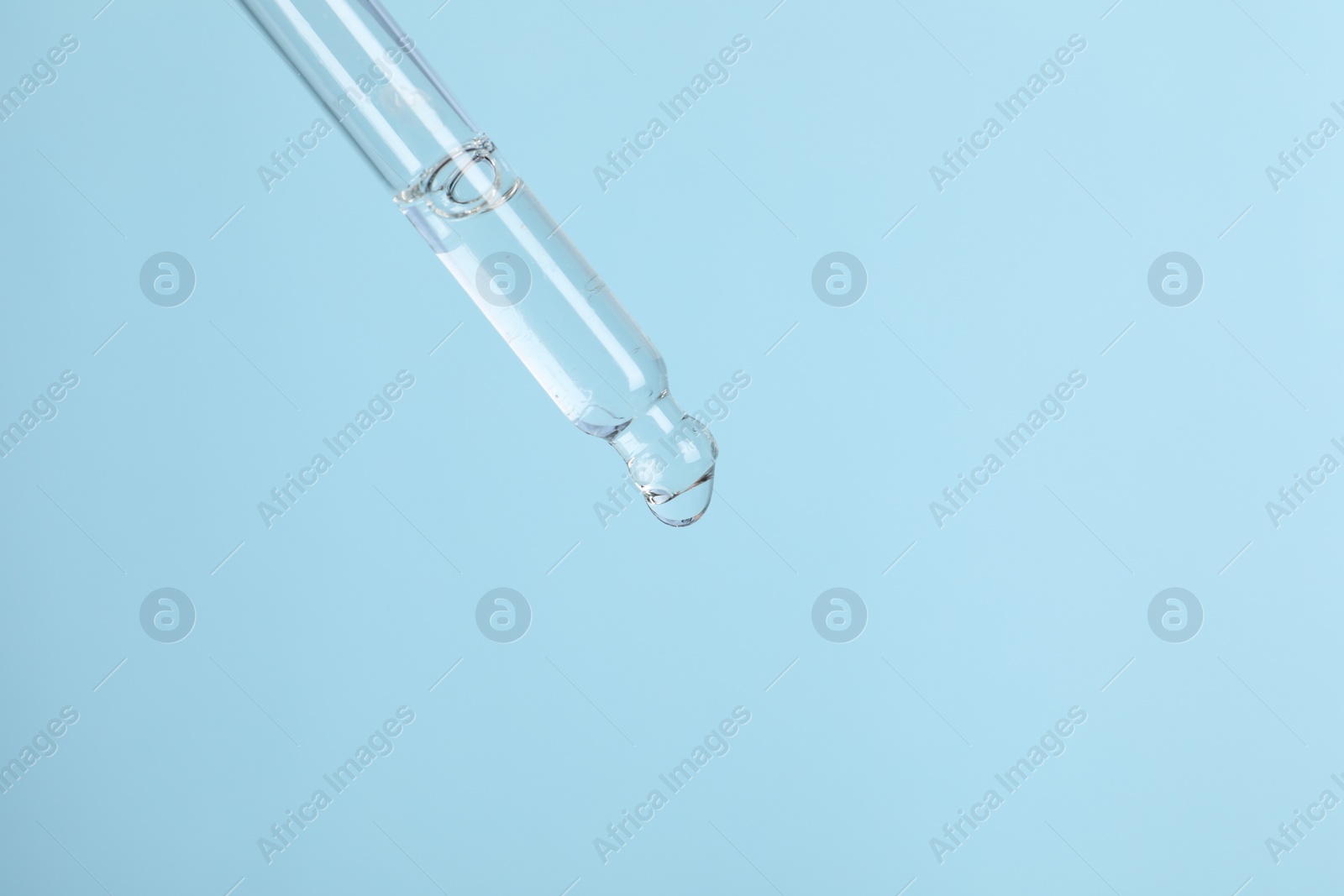 Photo of Dripping cosmetic serum from pipette on light blue background, space for text
