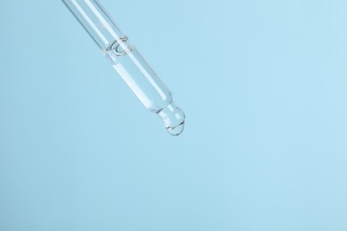 Photo of Dripping cosmetic serum from pipette on light blue background, space for text