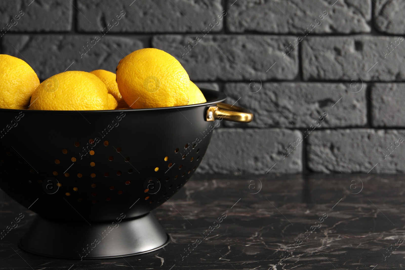 Photo of One colander with fresh lemons on black marble table, space for text