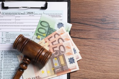 Tax return form, euro banknotes and gavel on wooden table, top view