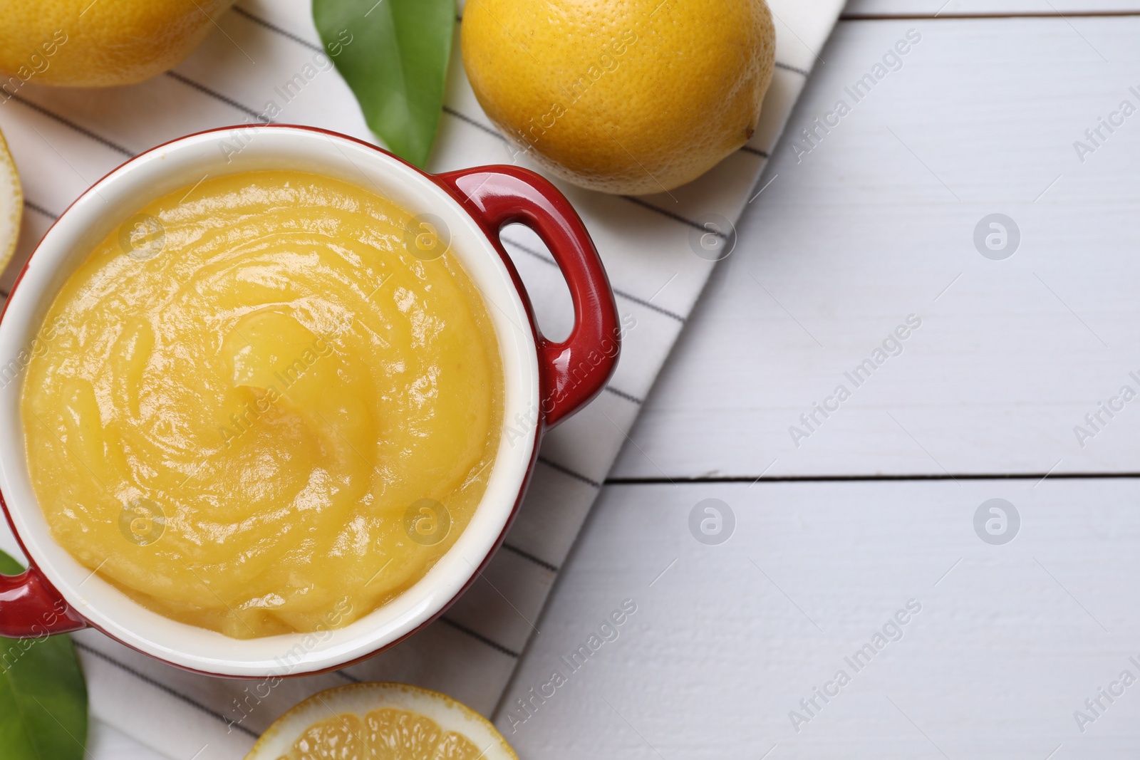 Photo of Delicious lemon curd in bowl and fresh citrus fruits on white wooden table, flat lay. Space for text