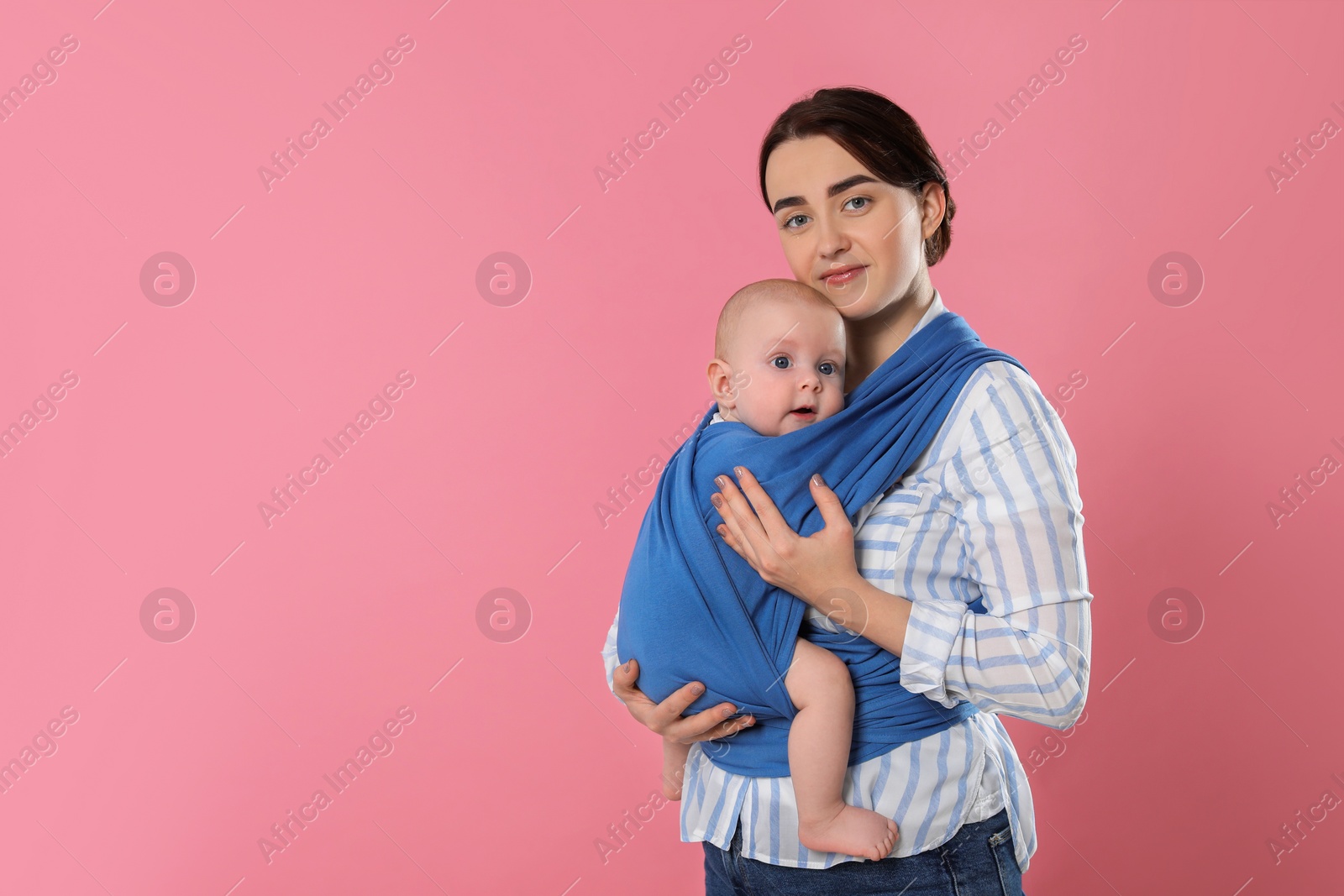 Photo of Mother holding her child in sling (baby carrier) on pink background. Space for text