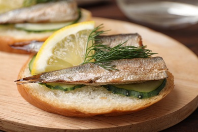 Photo of Delicious sandwich with sprats, cucumbers, lemon and dill on wooden board, closeup