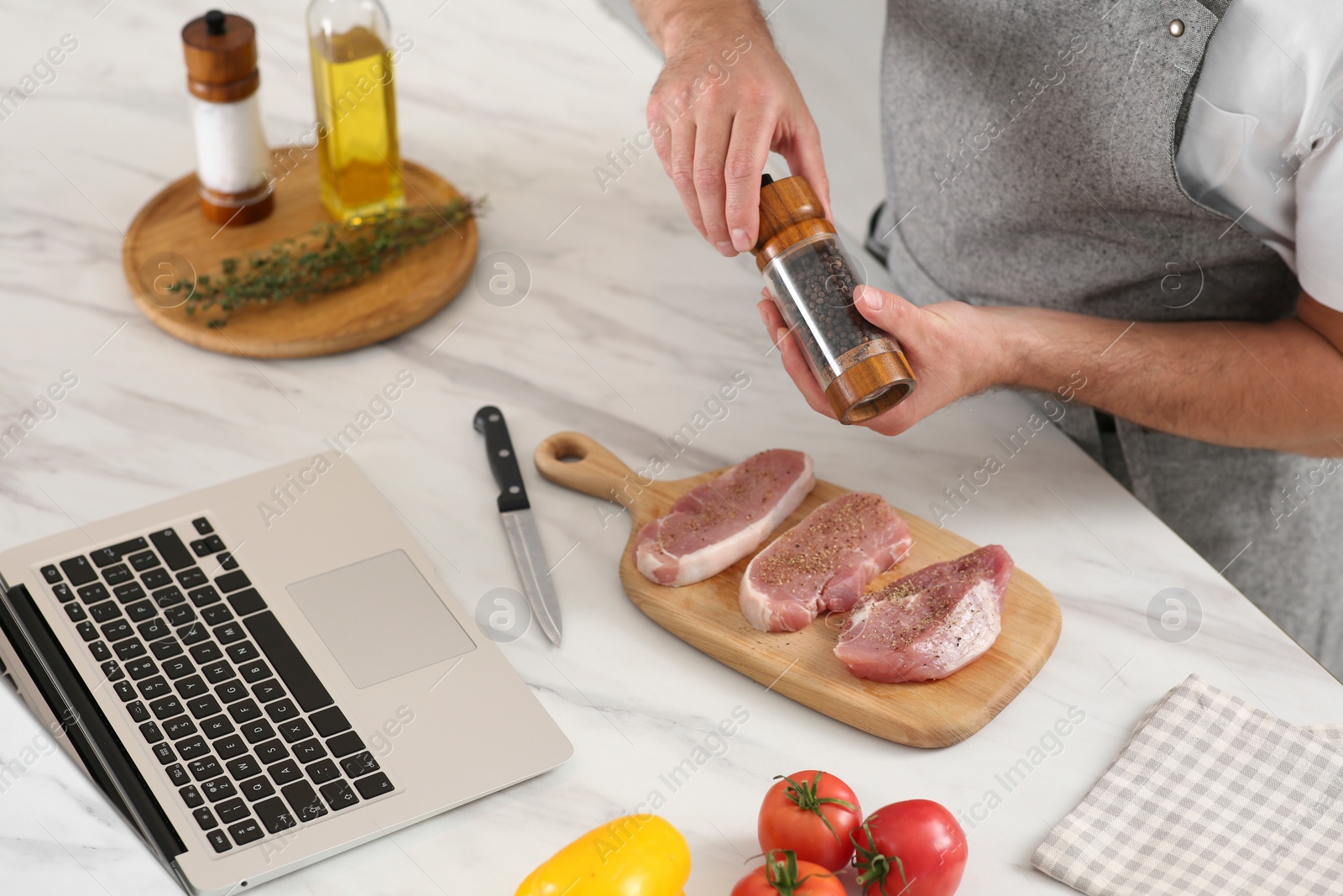 Photo of Man making dinner while watching online cooking course via laptop in kitchen, closeup