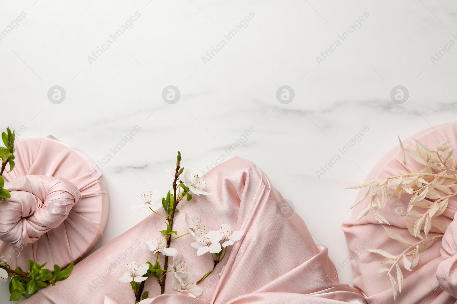 Photo of Furoshiki technique. Gifts packed in pink fabric on white marble table, flat lay. Space for text