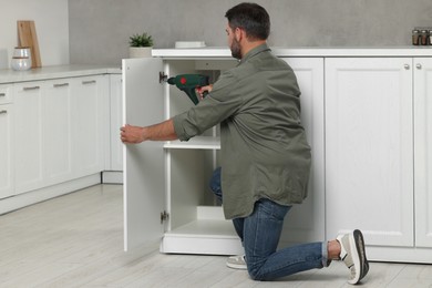 Photo of Man with electric screwdriver assembling furniture in kitchen