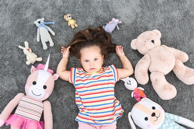 Photo of Cute little girl and soft toys on floor, top view