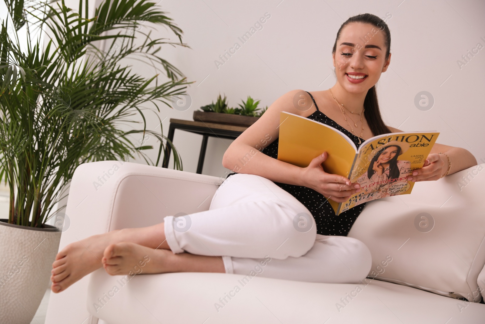 Photo of Happy woman reading magazine on sofa at home