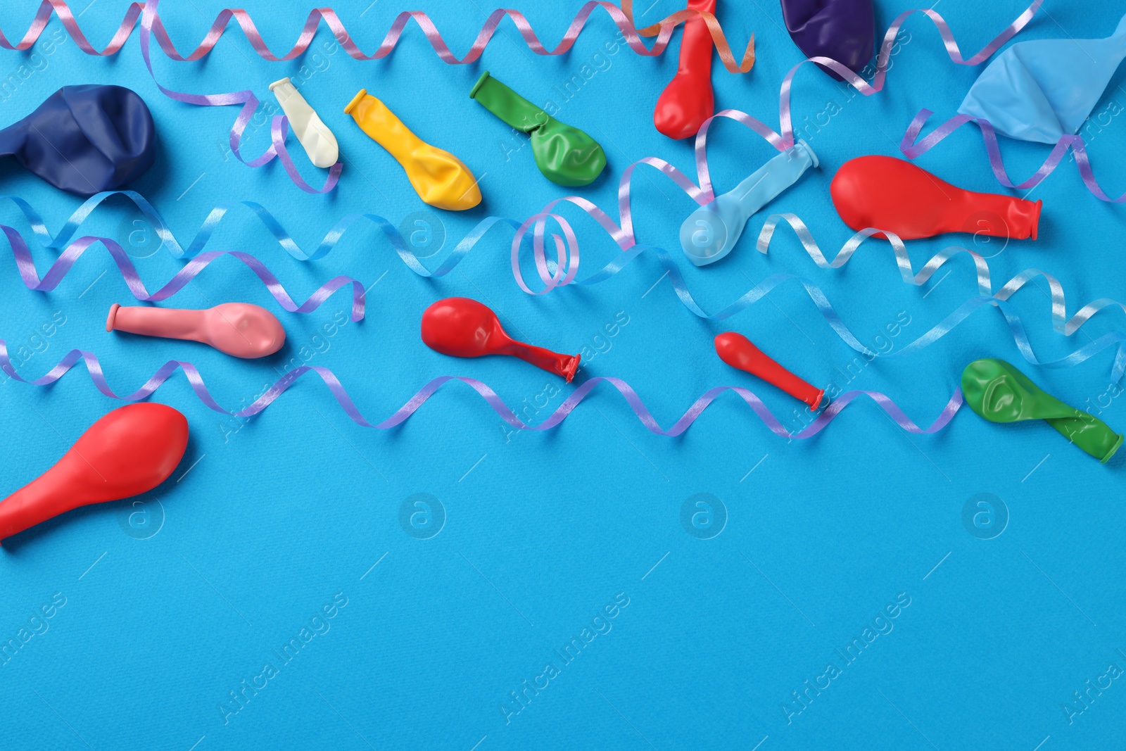 Photo of Colorful serpentine streamers and balloons on light blue background, flat lay