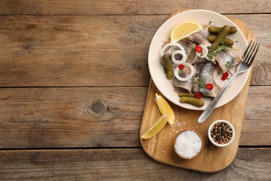 Salted herring fillets served with thyme, pickles, onion rings, chili pepper and lemon on wooden table, top view. Space for text