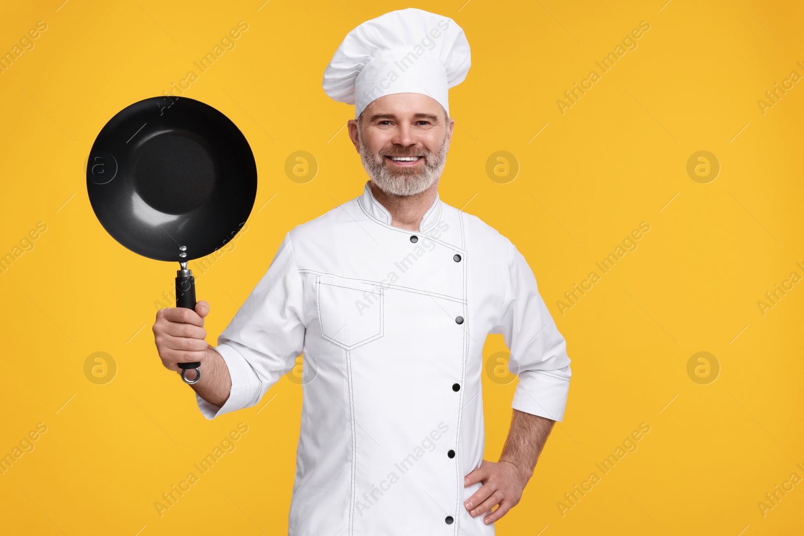 Photo of Happy chef in uniform with wok on orange background