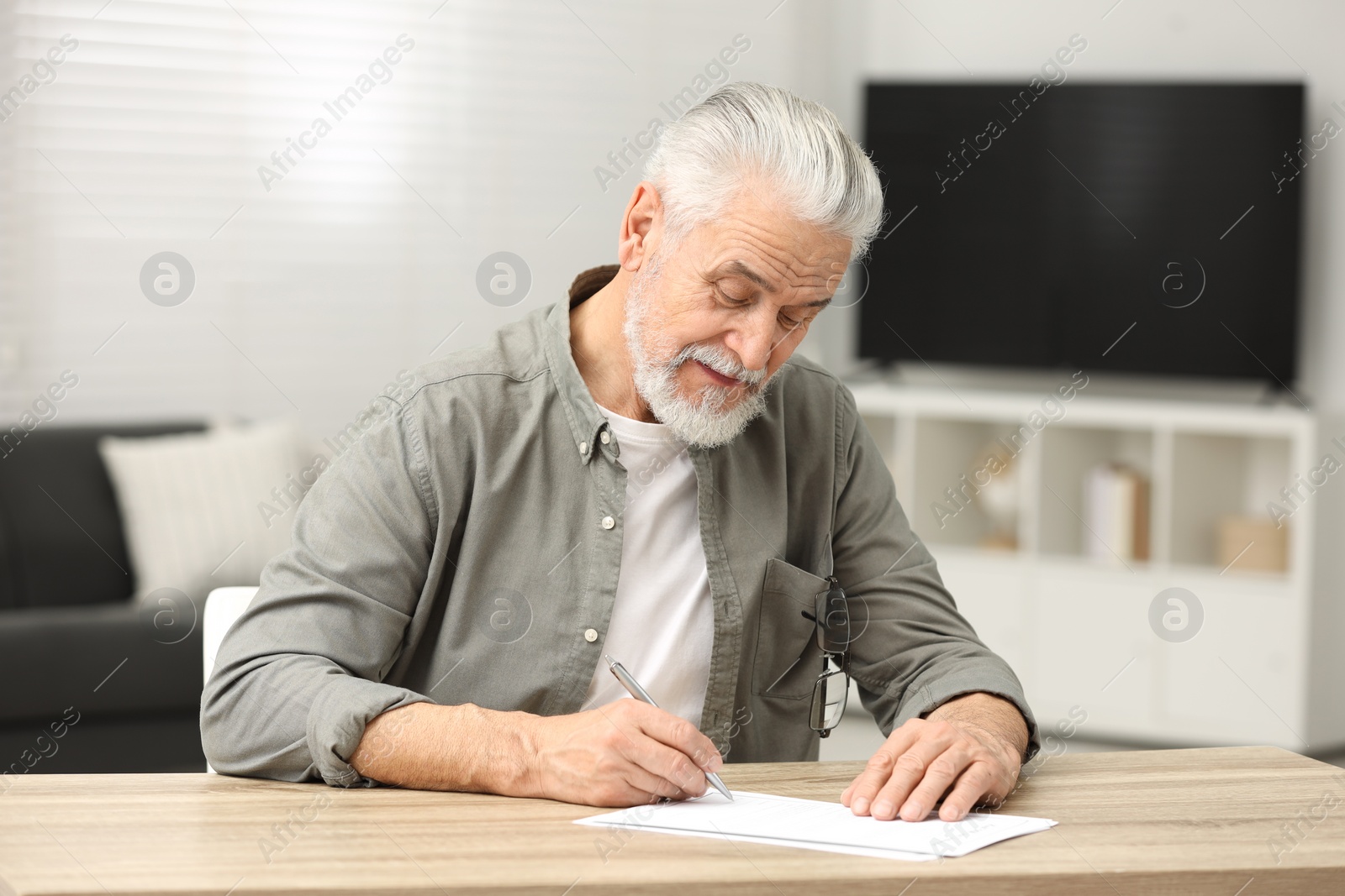 Photo of Senior man signing Last Will and Testament at table indoors