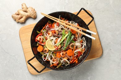 Photo of Shrimp stir fry with noodles and vegetables in wok on grey table, top view
