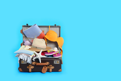 Photo of Packed vintage suitcase with different beach objects on light blue background, space for text. Summer vacation