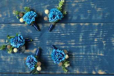 Photo of Stylish boutonnieres on blue wooden table, flat lay. Space for text