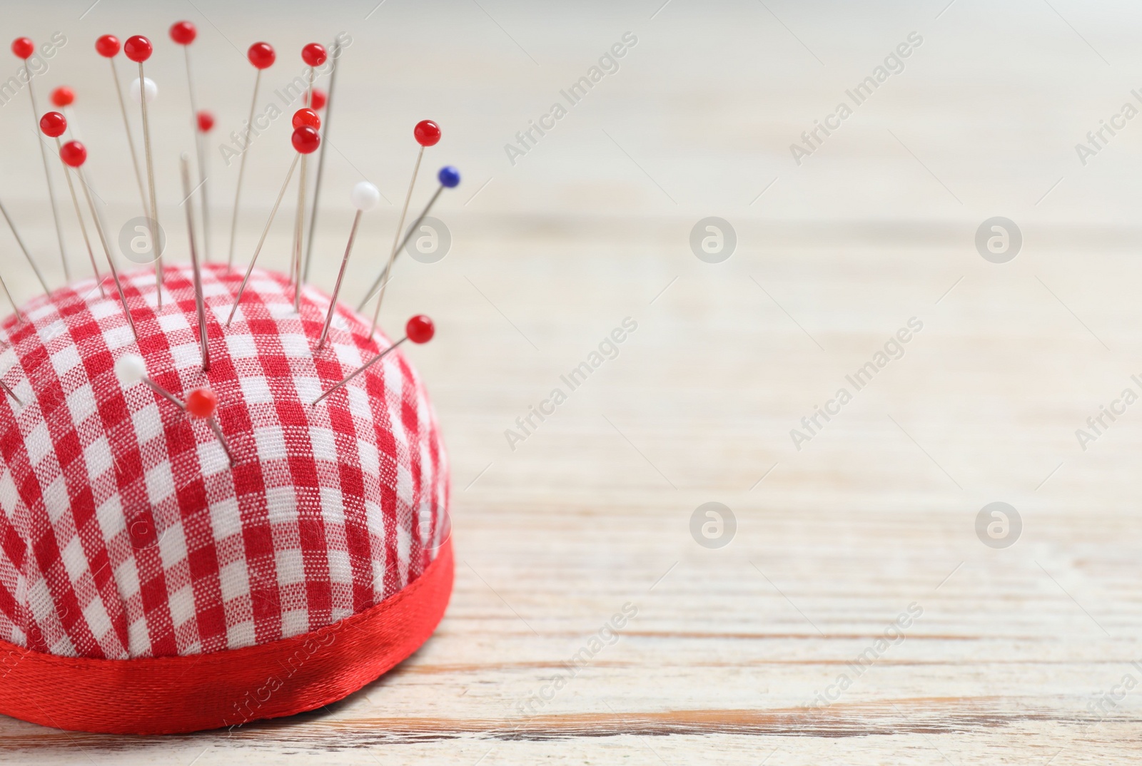 Photo of Checkered pincushion with sewing pins on light wooden table, closeup. Space for text