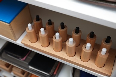 Photo of Wooden puzzle with cylinders and sockets near other montessori toys on shelves