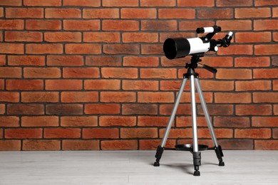 Tripod with modern telescope near brick wall. Space for text