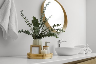 Vase with eucalyptus branches and toiletries near vessel sink in bathroom, space for text. Interior design