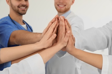 Photo of Team of medical workers holding hands together on light background, closeup. Unity concept